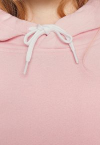 Sudadera rosa de tejido texturizado, con un cordón de ajuste blanco. El cuello es suave y ceñido, lo que mejora la calidez y la comodidad.