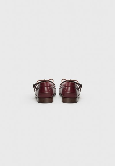 Mocasines de cuero burdeos con punta redondeada, costuras decorativas y acentos de cordones marrones. Suela de goma plana con un ligero tacón.