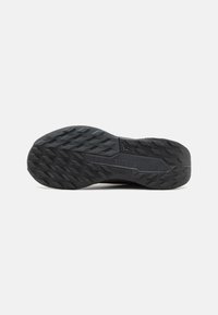 Semelle de chaussure de sport noire avec un motif texturé, présentant des rainures profondes et un logo Nike Trail. Fabriqué en matériau en caoutchouc durable pour une bonne adhérence.