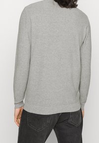 Pull gris à manches longues, col rond et poignets côtelés ; associé à un jean noir avec un design de poches en forme de cœur.