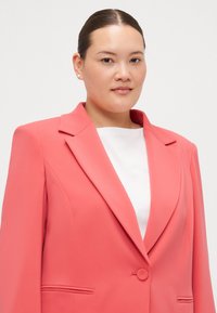 Koral blazer med notched lapels, enkel knappelukking og to frontlommer. Den glatte teksturen og den skreddersydde passformen gir en strukturert silhuett.