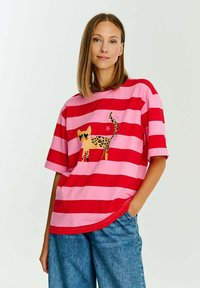 Červené a růžové pruhované tričko s grafikou kočky s leopardím potiskem. Krátké rukávy, volný střih, hladká látka a zakřivený spodní lem.