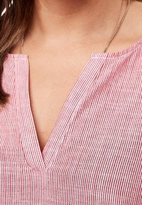 Tissu rayé rouge et blanc avec un col en V et une texture subtile. Présente des lignes verticales et une coupe décontractée.