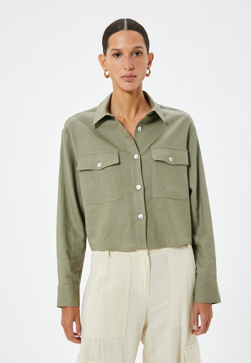 Camicia nelle tonalità di verde oliva, tagliata e con bottoni, dotata di taschini sul petto, realizzata in un tessuto leggero e con bottoni argentati. Maniche lunghe con dettagli ai polsini.