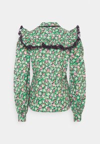 Blouse verte à fleurs manches longues avec fleurs roses, détail d'un volant en dentelle noire sur le haut du dos et les manches, poignets boutonnés.