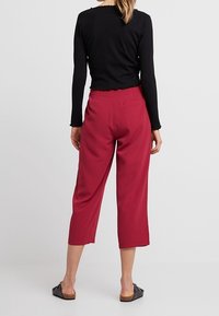 Haut noir à manches longues côtelé associé à un pantalon bordeaux taille moyenne, jambes larges, à la texture lisse et avec un détail de poche arrière.