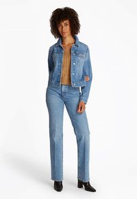 Svjetlo plava jeans jakna s gumbima sprijeda, džepovima na prsima i klasičnim krojem. Uparjena sa bež pletenim topom i svjetlo plavim trapericama. Crne čizme s potpeticom.