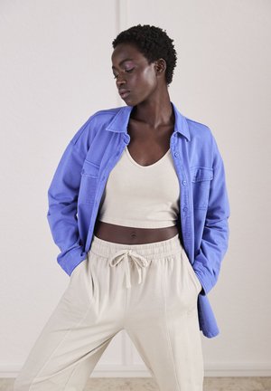 Lichtblauw overhemd met knopen, beige tanktop en beige sweatpants met elastische tailleband. Soepele texturen, casual stijl, relaxte pasvorm.