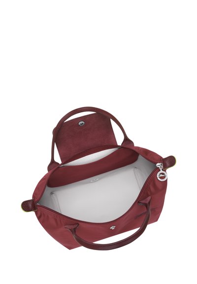 Bordeauxfarbene Tragetasche mit strukturiertengriffen, offenem Oberteil und einer Reißverschlusstasche innen. Gefüttert mit hellgrauem Stoff und mit einem Druckknopfverschluss.