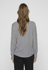 Long-sleeve blouse featuring vertical navy and white stripes, a rounded hem, and buttoned cuffs, made from lightweight fabric.