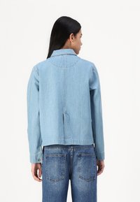 Lyseblå denimjakke med krage, lange ermer og en litt løs passform, med bakventil og minimale sømdetaljer.