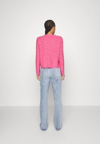 Magenta stickad tröja med ett texturerat mönster, cropped längd och långa ärmar, tillsammans med ljusblå vida jeans.