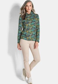 Langärmliges Oberteil mit einem Paisley-Muster in Grün, Blau und Gelb, kombiniert mit beigen Hosen und beigen Sneakern. Glattes, elastisches Material.