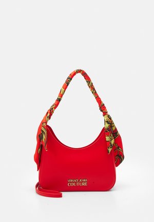 Rote Schultertasche mit goldenem "Versace Jeans Couture"-Logo und einem mit gemustertem Stoff umwickelten Griff mit roten, gelben und schwarzen dekorativen Designs.