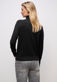 Maglione nera a maglia con colletto alto e maniche lunghe; presenta un design aderente e orlo a costine. Abbinato a jeans chiari, strappati.