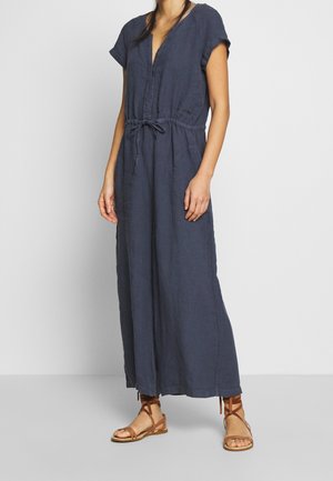 Navy blue linen maxi dress with short sleeves, V-neck, belt tie at the waist, and two side pockets; worn with brown strappy sandals.