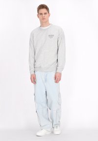 Grå sweatshirt med rund hals, der har et lille sort grafisk motiv. Lyseblå cargo-bukser med flere lommer. Hvide sneakers.