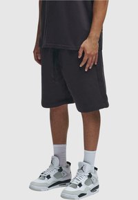 Shorts en coton noir avec une taille élastique et un cordon de serrage, associés à des baskets blanches et noires avec des détails en mesh.