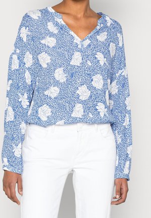 Blauwe bloemen blouse met lange mouwen en een V-hals ontwerp, met witte bloempatronen en een losse pasvorm. Gecombineerd met witte broek.