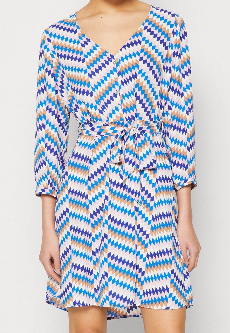 Gemustertes Kleid mit V-Ausschnitt, langen Ärmeln und gebundenem Taillengürtel. Der Stoff zeigt ein geometrisches Design in blau, lila und orange Farbtönen.
