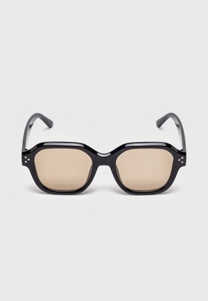 Czarne prostokątne okulary przeciwsłoneczne z grubymi oprawkami i jasno-brązowymi przyciemnianymi szkłami, prezentowane na białym tle.