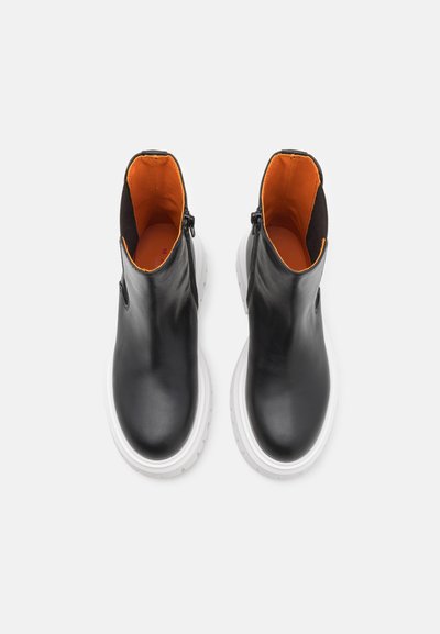 Botas de cuero negras hasta el tobillo con forro naranja, que cuentan con una cremallera lateral, punta redonda y suela de plataforma blanca. Textura suave con un diseño simple.