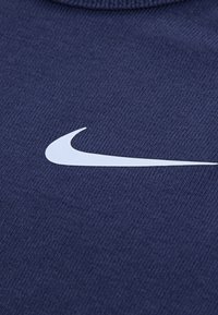 Tmavomodrá pletená látka so zreteľným bielym logom Nike swoosh. Textúra je hladká s jemnými horizontálnymi ryhami.