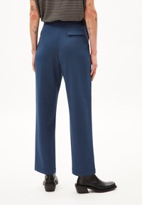 Navyblauwe broek met een relaxte pasvorm, voorzien van een achterzak en subtiele textuur. Gestyled met zwarte haklaarzen, gezien van achter.
