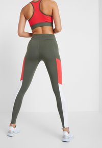 Grünes und rotes Sportoutfit bestehend aus einem Racerback-Top und farblich abgesetzten Leggings mit weißen Akzenten, entworfen für Komfort bei sportlichen Aktivitäten.