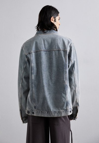 Light blue denim jacket with a relaxed fit, visible seams, and buttons at the cuffs. Features a classic collar and back yoke design.