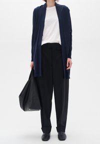 Cárdigan azul marino, camisa blanca y pantalones de tiro alto negros. Bolso de cuero negro. Tejido suave, corte relajado y silueta estilizada.