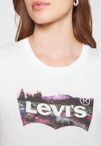 Biały bawełniany t-shirt z kolorową grafiką krajobrazu górskiego oraz wyraźnym logo "Levi's" w pogrubionych białych literach.