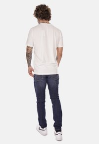 T-shirt bianco a maniche corte, jeans blu e sneakers bianche visti da dietro. Il T-shirt ha una texture liscia; i jeans sono attillati e in denim.