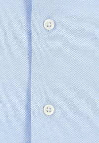 Camicia testurizzata azzurro chiaro con una sottile trama a righe, rifinita con due bottoni bianchi sullo scollo. Il tessuto ha una trama sottile.