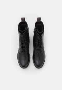 Un par de botines negros de cuero con cordones y cremalleras laterales, vistos desde arriba sobre un fondo blanco.