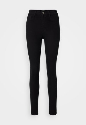 Svarte høyhalsede skinny jeans laget av denim. Har fem lommer og en metallknapp foran. Glatt tekstur med en tettsittende design.