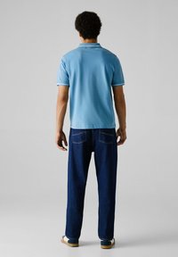 Svetlomodrá polokošeľa s krátkymi rukávmi a golierom, doplnená o tmavomodré rovné džínsy. Tento outfit sa vyznačuje nenápadnými detailmi.