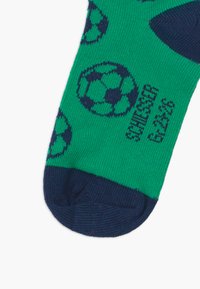 Chaussettes vertes avec des accents bleu marine, ornées d'un motif de ballons de football noirs et blancs. Fabriquées en tissu tricoté avec une texture douce.
