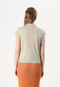 Lys beige kortermet topp med rund halslinje, med en jevn tekstur. Kombinert med en tettsittende oransje ribbestrikket skjørt.