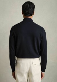 Mornarsko pleteni pulover z visokim ovratnikom, dolgimi rokavi in slim fit krojem, v kombinaciji s kremnimi hlačami z detajlom na zadnjem žepu.