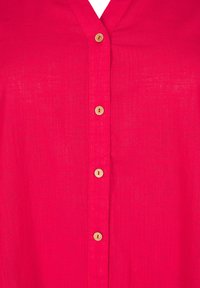Rosa skjorta med knappar i en texturerad tyg, med V-urringning och fem träknappar fram.