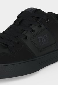 Baskets basses noires avec des lacets épais, une semelle texturée et un logo DC brodé sur le côté et la languette.