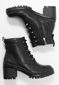 Mustat nahkaiset nilkkurit, joissa on teksturoitu pinta, nyöritys edessä, sivuvetoketju ja paksu, iskuja vaimentava pohja; ominaisuuksina kerrostettu korko ja vetolenkki.