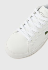 Λευκό δερμάτινο αθλητικό παπούτσι με στρογγυλεμένη μύτη, επίπεδα κορδόνια και πράσινο κεντητό λογότυπο στο πλάι. Ελαστική σόλα με υφή.