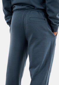 Dunkelblaue Sweatpants aus weichem Stoff, mit einem elastischen Bund und einer Gesäßtasche mit schmaler Öffnung. Glatte Textur.