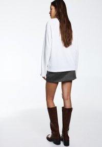 Stivali al ginocchio in pelle marrone con tacco spesso abbinati a una gonna grigia e a una felpa bianca, che mostrano uno stile casual stratificato.