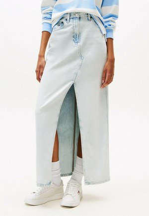 Lichtblauwe denimmaxi-rok met een voorzichtige split, met een hoge taille, knoopsluiting en subtiele vervaging; gecombineerd met witte sneakers en sokken.