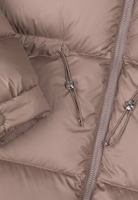 Kurtka puchowa w jasnobrązowym kolorze o gładkiej fakturze, wyposażona w przedni zamek błyskawiczny, ściągacze z troczkami oraz metaliczne guziki jako akcenty.