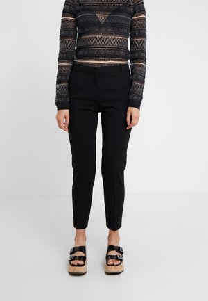 Pantalons noirs ajustés avec une coupe slim, associés à un haut à manches longues noir et crème à motif texturé, et des sandales compensées avec boucles.