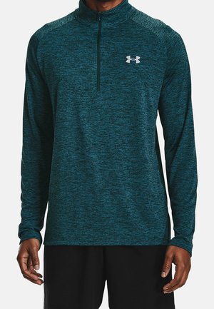 Man wearing a teal, long-sleeve, quarter-zip athletic pullover with a white Under Armour logo on the chest.